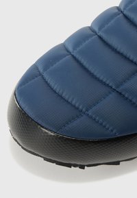 Dessus matelassé bleu avec une texture lisse, associé à une semelle en caoutchouc noir dotée d'une surface à motif pour une meilleure adhérence.