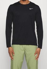 Schwarzes Nike-Shirt mit langen Ärmeln und rundem Ausschnitt, aus glattem Stoff, mit einem weißen Logo auf der linken Brust.