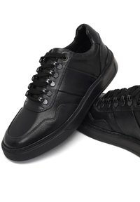 Baskets en cuir noir avec une finition lisse, dotées de six œillets, de lacets plats noirs et d'une semelle extérieure en caoutchouc texturé. Agrémentées de lignes cousues.