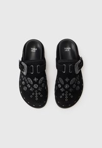 Clogs negre tip slip-on cu ținte decorative negre și o curea mare cu cataramă, etichetate "TOGA VIRILIS" în interiorul tocului.