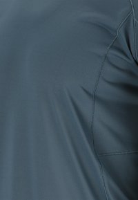 Tumman teal värinen lyhythihainen paita, joka on tehty kevyestä, teksturoidusta kankaasta. Siinä on sileät saumat ja hienovarainen hengittävä kuvio pinnalla.