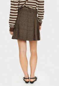 Woman wearing a brown plaid pleated skirt, a brown and white striped long-sleeve top, and black flat sandals, shown from the back.