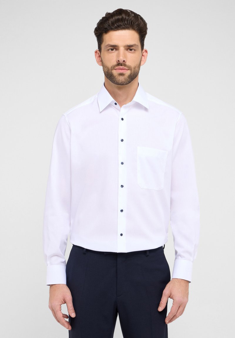 Weißes Langarmshirt mit einem Button-Down-Kragen, ausgestattet mit einer einzelnen Brusttasche und dunklen Knöpfen auf einem glatten Stoff.