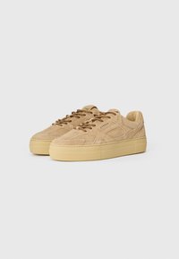 Beige sneakers i semsket skinn med tykk såle, rund tå og sømdetaljer. Brune snøringer og subtil merkevare på tungen fullfører designet.