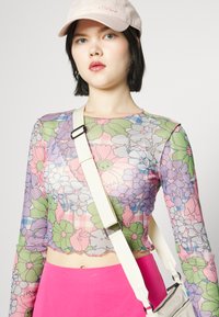 Camisola de manga longa transparente com um padrão floral colorido em rosa, verde e azul. Apresenta um corte cropped e uma bainha sutilmente recortada.