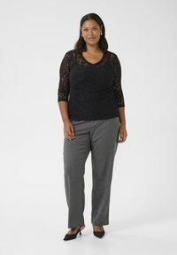Haut en dentelle noire à manches trois-quarts, associé à un pantalon gris taillé. La tenue présente un décolleté en V et des talons noirs élégants.