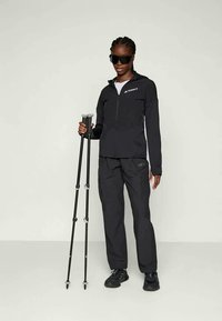 Mustam välistingimustes jope, millel on tõmblukuga ees, koos sobivate cargo-pükstega ja matkakeppidega. Aktsentideks on valge brändi logo.