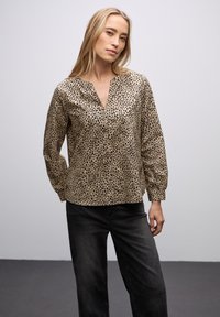 Leopardmønstret bluse i beige med v-hals, lange ærmer og subtil glans. Parret med mørk denim jeans for kontrast.