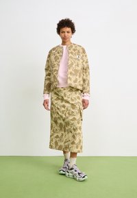 Camo-patterned jacket and skirt set in beige with pink accents. Athletic shoes with gray and mint details. Smooth fabric texture.