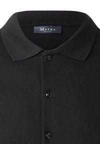 Polo shirt nera con colletto a coste, patta con quattro bottoni neri e un morbido tessuto a maglia testurizzato.