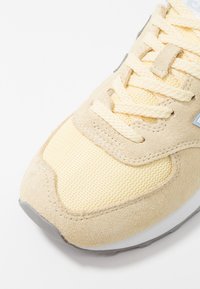 Lys gul sportssko med mesh-overdel, ruskindsdetaljer, runde snørebånd og grå gummisål med et tekstureret mønster på overfoden.