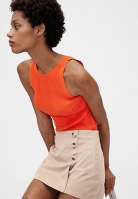 Lyseorange, ribbet ærmeløs top parret med en lysebeige, højtaljet nederdel med fem cremeknapper og en sideslidsdetalje.