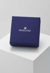 Mørkeblå teksturert smykkeboks med en glatt finish, med et hvitt Swarovski-logo og svanedetalj på forsiden, i firkantet form.