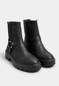 Black ankle boots made of smooth synthetic material, featuring a side zipper, elastic panels, and a chunky sole with a textured grip.