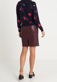 Marinblå tröja med blommig brodyr i röd och blå, tillsammans med en bordeauxfärgad läderkjol. Svarta skor med blockklack fulländar outfiten.