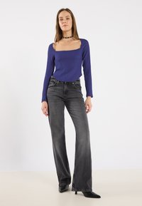 Top blu ribbed a maniche lunghe con scollo quadrato, abbinato a jeans a gamba larga grigi a vita alta e tacchi a punta neri.