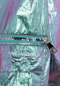 Tkanina o srebrzystym, metalicznym odcieniu z pomarszczoną fakturą; kieszeń na zamek z kwadratowymi detalami; logo "KARL LAGERFELD" w białym kolorze.