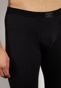 Melni kokvilnas stiepļu biksītes ar pieguļošu dizainu, kas piedāvā ciešu jostasvīru un priekšējo kabatu. Vienkārša šūšana, minimāla zīmola identifikācija.