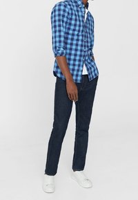 Niebieska i czarna koszula w kratę z guzikami, z podwiniętymi rękawami, w zestawieniu z ciemnymi dżinsami i białymi trampkami. Prosty design i bawełnowa tekstura.