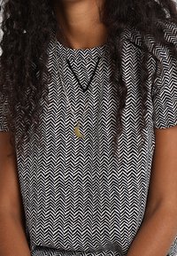 Camisa de manga corta con un patrón de zigzag en blanco y negro, con un escote redondo. Un collar de media luna dorada es visible.