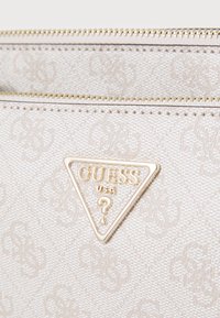 Tasche aus strukturiertem, hellbeigem Stoff mit einem goldenen, dreieckigen Logo und einem Reißverschluss. Dezentes Muster, das auf dem Material geprägt ist.