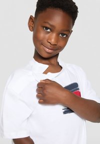 Weißes kurzärmliges T-Shirt mit einem bunten Pinselstrichdesign in Marineblau und Rot. Der Stoff scheint weich und bequem zu sein.