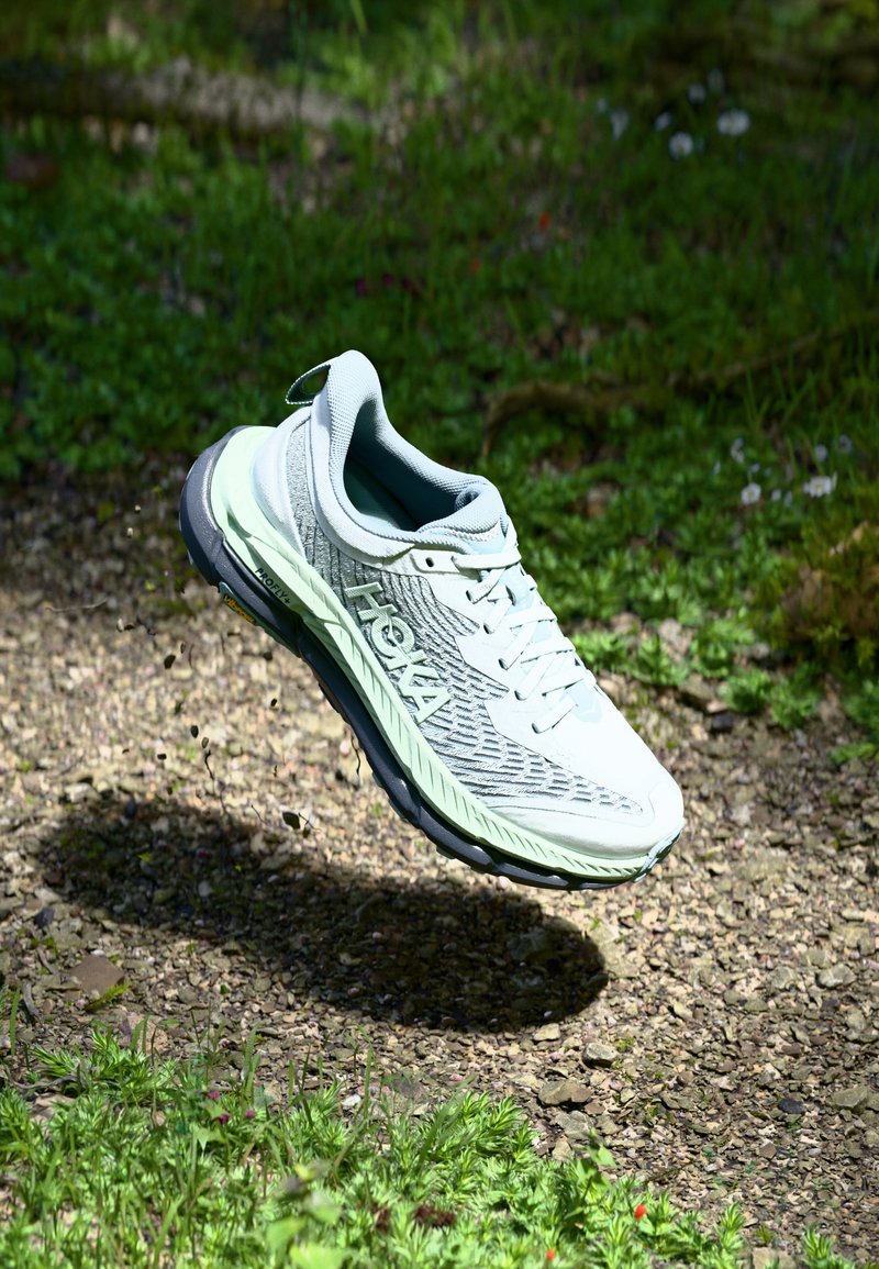 Vaaleanharmaat juoksukengät, joissa on teksturoitu päällinen, verkkosuunnittelu ja mintunvihreät yksityiskohdat. Varustettu pehmeällä pohjalla ja heijastavalla logotiedolla.