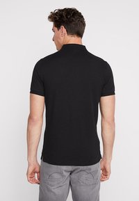 Sort polo-shirt, korte ærmer, glat stof, klassisk krave, let design. Båret med lyse grå jeans med stikning på lommerne.