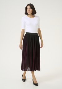 Schwarzer Faltenrock mit bordeauxroten vertikalen Streifen, kombiniert mit einem eng anliegenden weißen Oberteil und schwarzen Slingback-Pumps mit spitzer Zehenpartie.