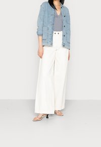 Jeansjacka med fickor, randig topp och vida vita byxor. Ljust blå och vit färgskala, strukturerad tyg och platta sandaler.