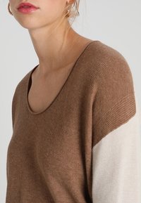 Braun- und cremefarbener farblich blockierter Pullover aus weichem Strick, mit einem weiten Ausschnitt und geripptem Muster an den Ärmeln. Legeres Design.