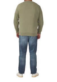 Felpa girocollo verde oliva con polsini e orlo a coste, indossata su jeans in denim blu, che mostra una vestibilità informale e linee pulite.