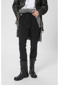 Személy fekete bőr köténycsizma, fekete nadrág, fehér ing, fekete bőr dzseki és szürke kötött pulóver, amely a csípő köré van kötve.