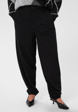 Pantalon noir ample associé à des chaussures noires à talons bas pointus, porté avec un pull à motifs.