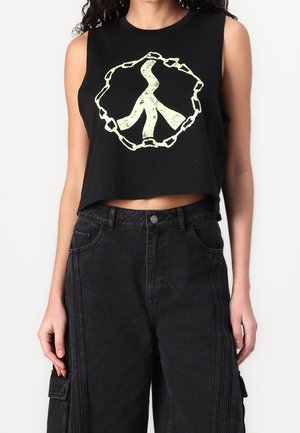 Sort cropped tank top med et lysende grønt fredssymbol omgivet af et kædedesign. Båret med højtaljede sorte denimbukser.