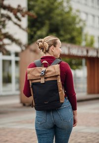 Batoh s hnědým horním klapkou se zámkem, černým tělem a děrovanými akcenty. Nastavitelné popruhy a elegantní obdélníkový tvar.