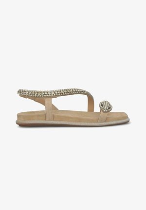 Sandal beige con un cinturino decorato da strass, suola piatta e un particolare elemento decorativo sulla punta. Texture liscia, design minimale.