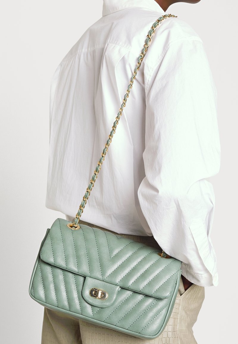 Borsa a spalla in pelle trapuntata verde con una tracolla in catena dorata, caratterizzata da una forma rettangolare, un coperchio flap e una chiusura a scatto.