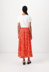 Witte top met korte mouwen, gecombineerd met een levendige rode maxirok met een bloemenpatroon in geel en zwart, met een elastische tailleband.