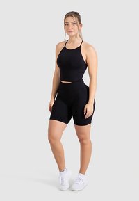 Schwarzes, eng anliegendes, sportliches Crop-Top und hoch taillierte Shorts aus elastischem Stoff, kombiniert mit weißen Sneakern. Schlichtes, nahtloses Design.