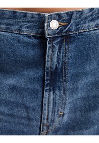 Džínové kalhoty s vysokým pasem, se stříbrným knoflíkem a oranžovým prošíváním. Látka má střední modrou barvu s mírně opotřebovanou strukturou.