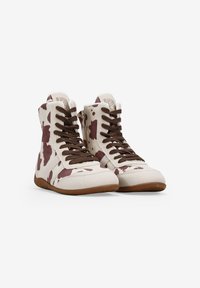 Zapatillas de caña alta con tela crema que presenta un estampado de vaca marrón. Cordones marrones y suela de goma. Detalle de cremallera en el lateral.