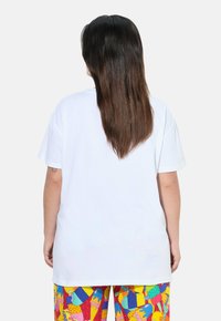 Camiseta de algodón blanca con un corte relajado, mangas cortas y un escote redondo, combinada con pantalones de patrón colorido.
