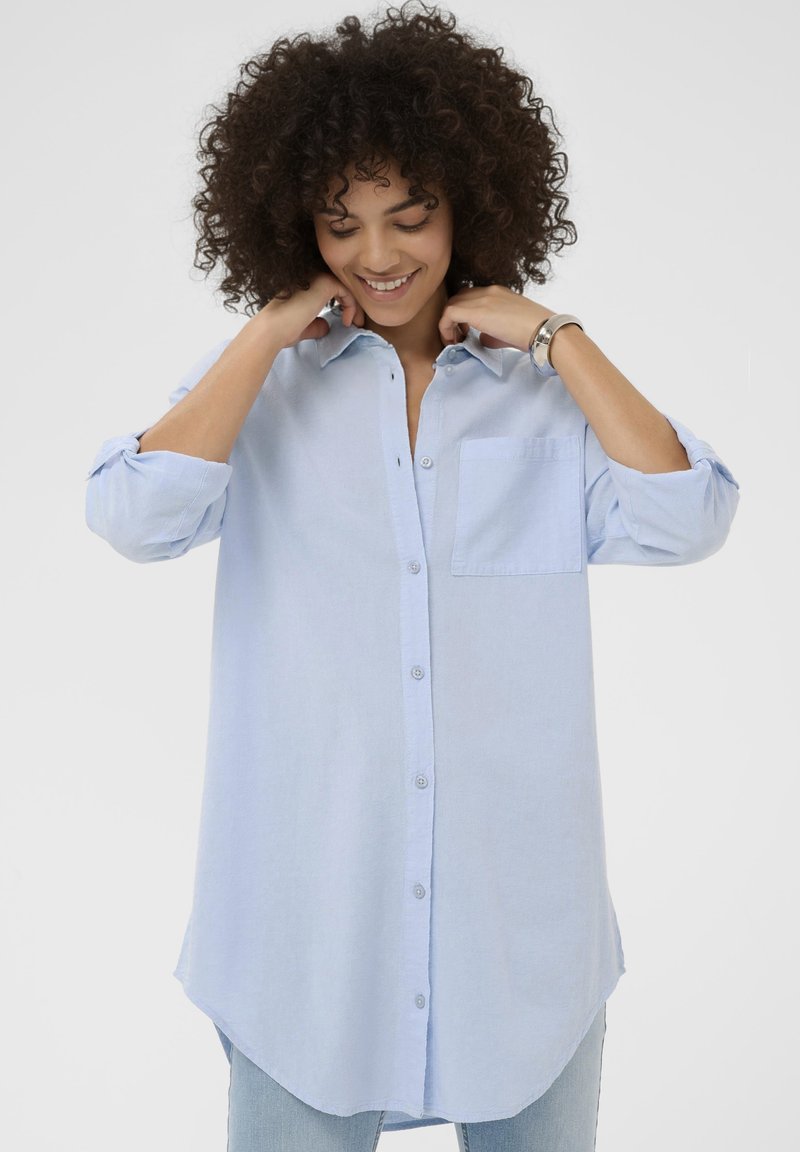 Hele sinine nööbitav särk tasku, rullitud varrukate ja kumerate servadega. Valmistatud pehmest kangast, lõdva lõikega.