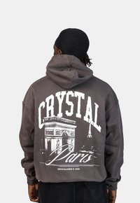 Šedá mikina s kapucí s velkým grafickým motivem Arc de Triomphe a Eiffelovy věže, doplněná textem "CRYSTAL Paris" v tučném bílém písmu.
