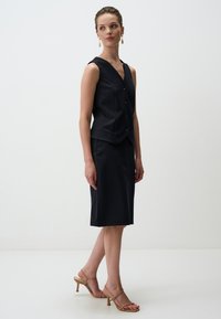 Ensemble de gilet et jupe à rayures marines, avec un décolleté en V, une fermeture à boutons et un design épuré. Associé à des talons beiges à lanières. Texture lisse.