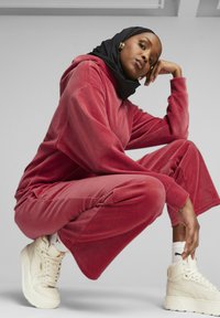 Czerwony dres z weluru z oversize'ową bluzą z kapturem i szerokimi spodniami. Białe trampki na platformie z teksturowanym wykończeniem. Czarna chusta i złote kolczyki w kształcie kół.