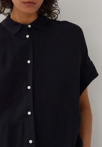 Camicetta blu navy a maniche corte con abbottonatura frontale, caratterizzata da un colletto classico e bottoni bianchi. Realizzata in un tessuto leggero e morbido.