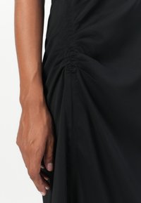 Black dress with ruched detailing on the side, featuring a smooth, lightweight fabric and a slim fit, highlighting subtle texture and drape.