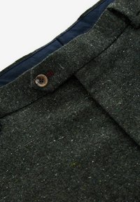 Dunkelgrüne Tweed-Hosen aus strukturiertem Stoff, mit einem Einzelknopfverschluss und kontrastierender blauer Taillenverarbeitung.